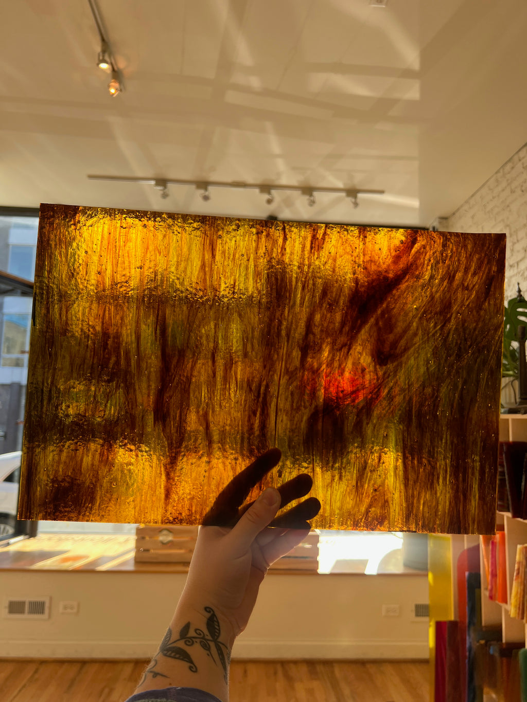 Hand holding a large swirled piece of glass with warm colors in an indoor setting.