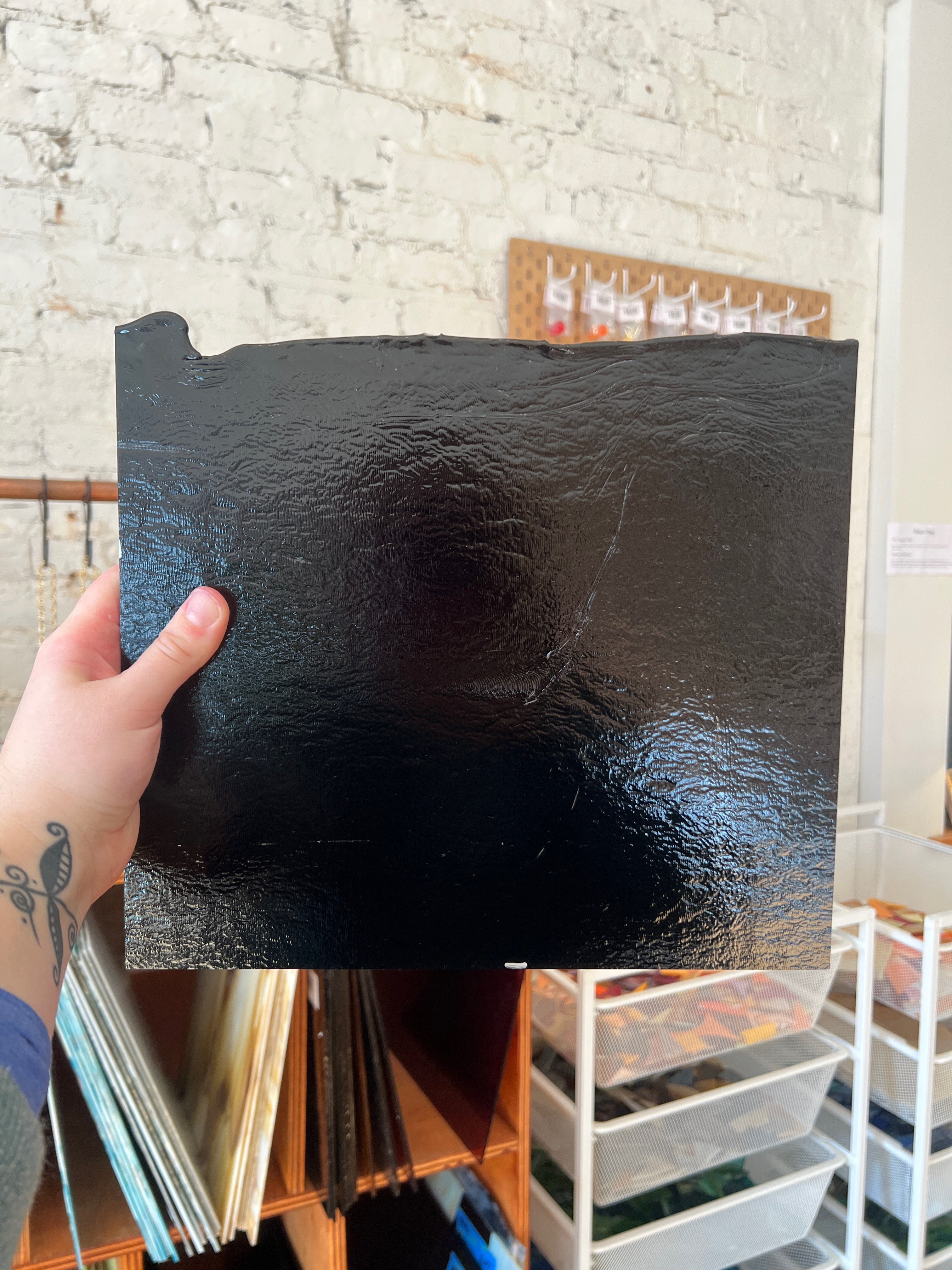 Person holding a textured black piece of stained glass against a white brick wall.