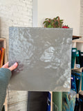 Person holding a textured gray piece of glass in a store setting