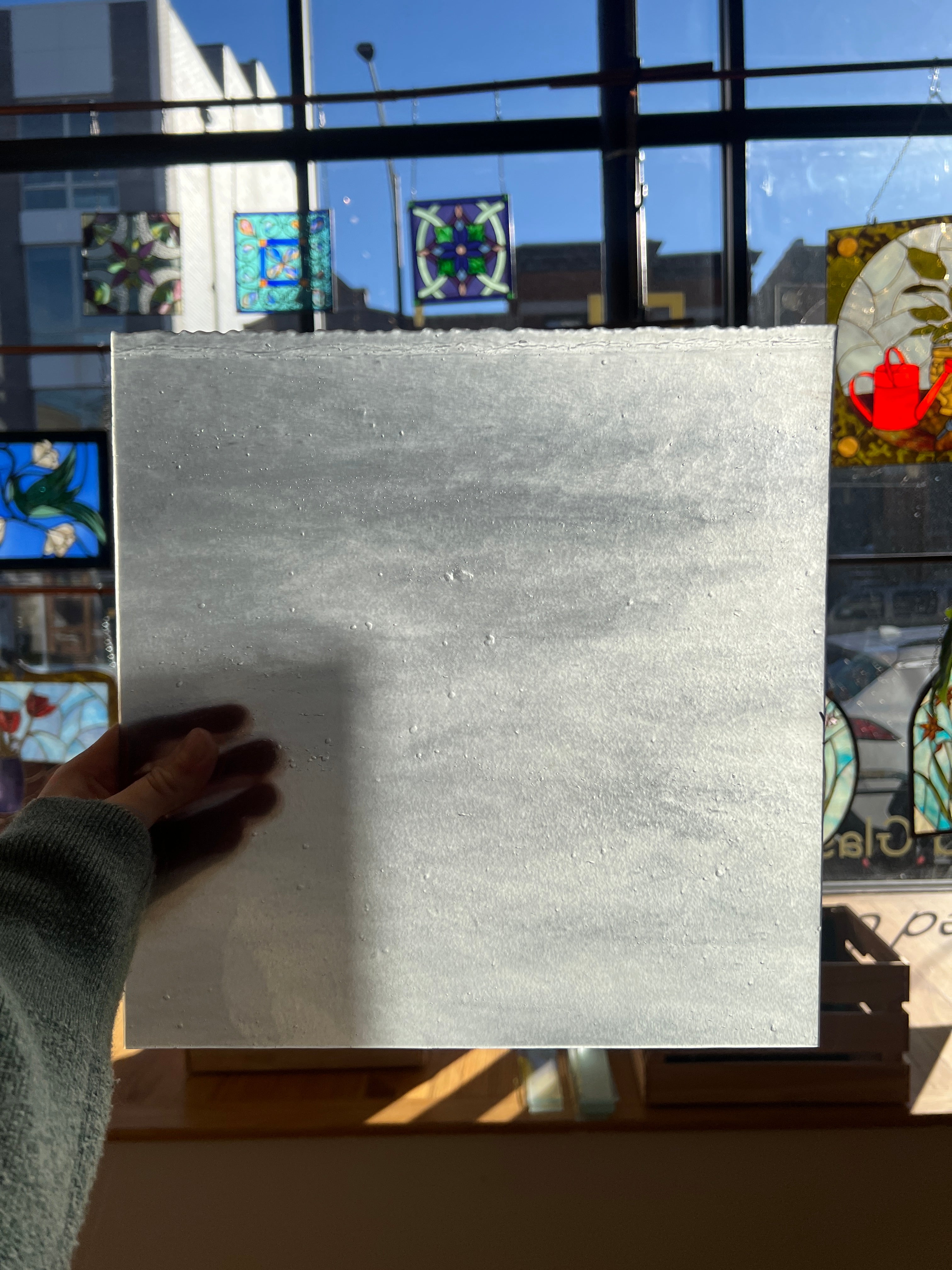 White sheet of textured glass held by a hand with stained glass windows in the background