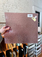 Person holding a piece of purple glass with a label against a brick wall.