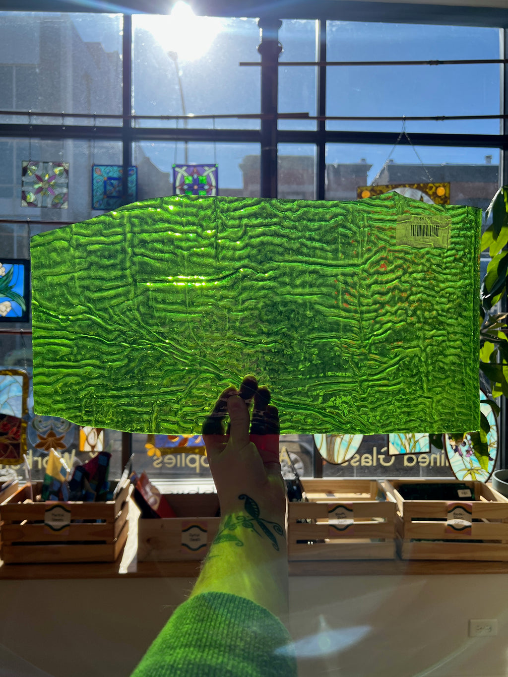 Green textured piece of stained glass held by a hand in front of a window with a cityscape view.