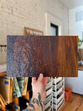 Person holding a textured brown piece of stained glass in a room with white brick walls and wooden floors.