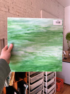 Person holding a green and white marbled piece of stained glass with a visible barcode against a room background.