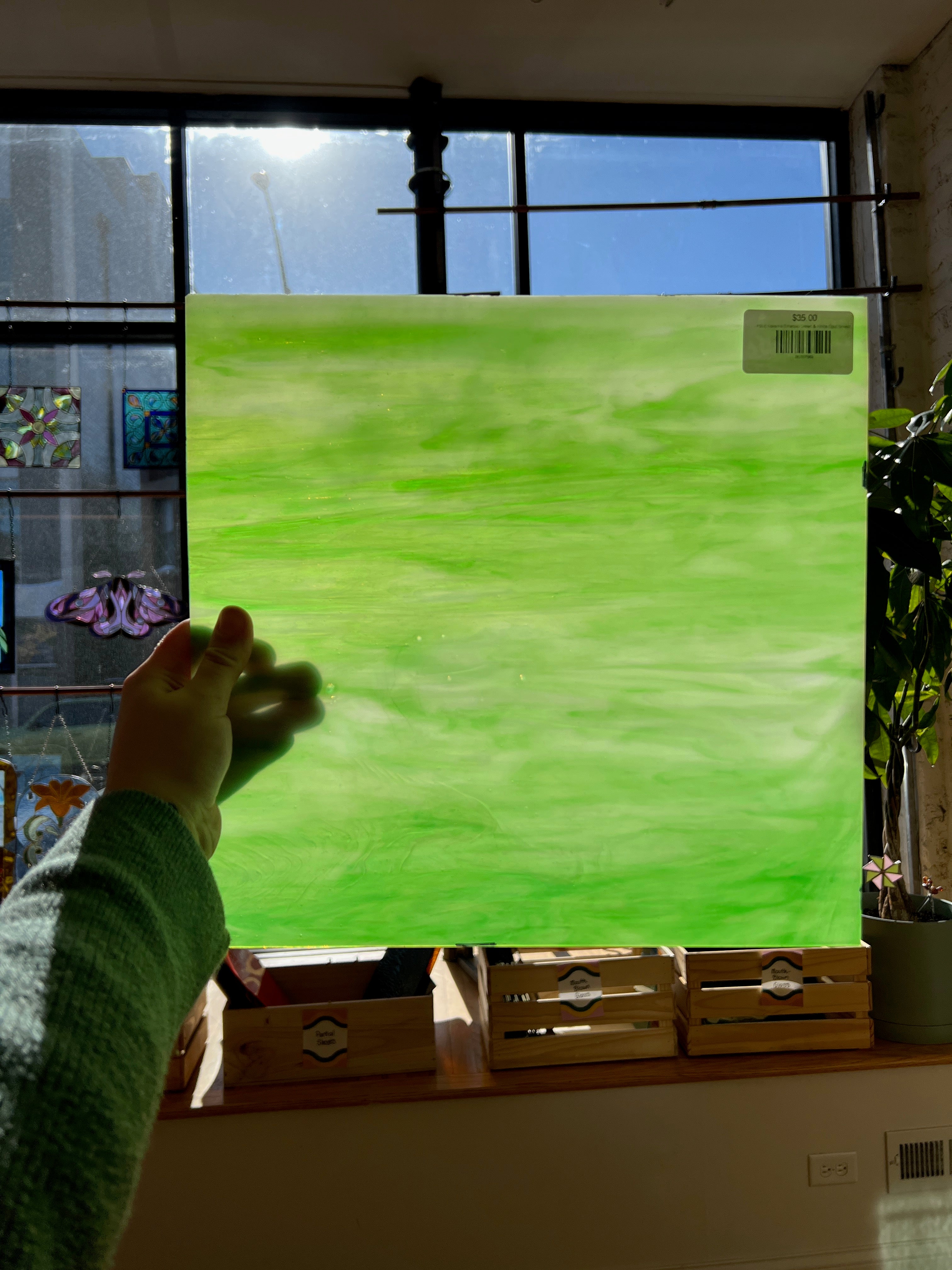 Person holding a green piece of stained glass in front of a sunny window 