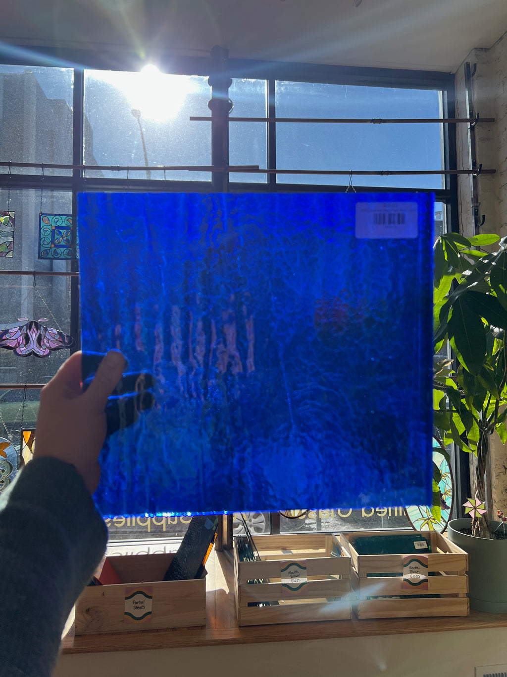 Person holding a blue textured piece of stained glass in front of a window