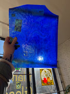 Hand holding a blue textured piece of glass with a blurred indoor background