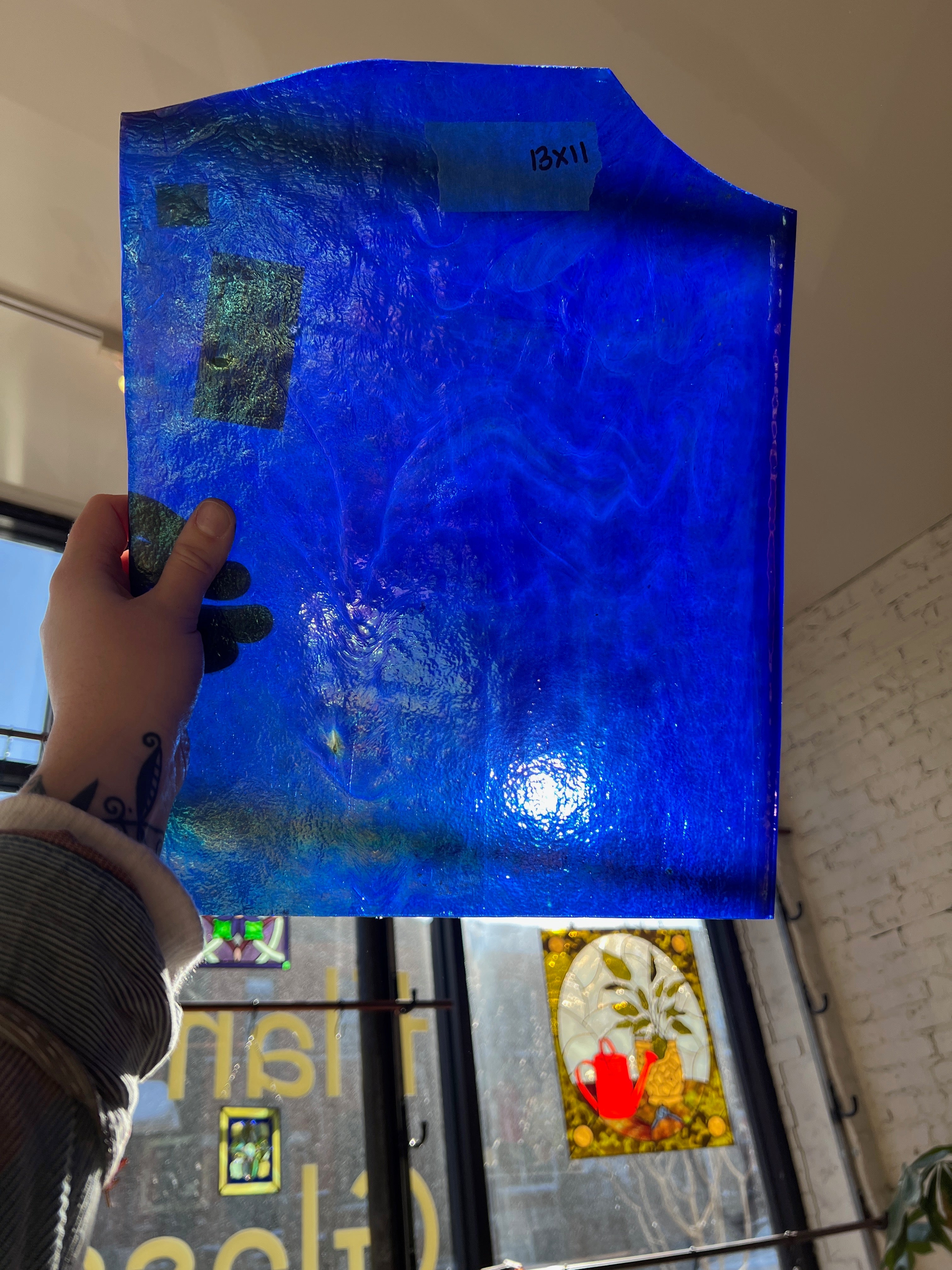 Hand holding a blue textured piece of glass with a blurred indoor background
