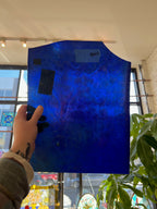 Blue textured piece of glass held by a person indoors with windows and plants in the background