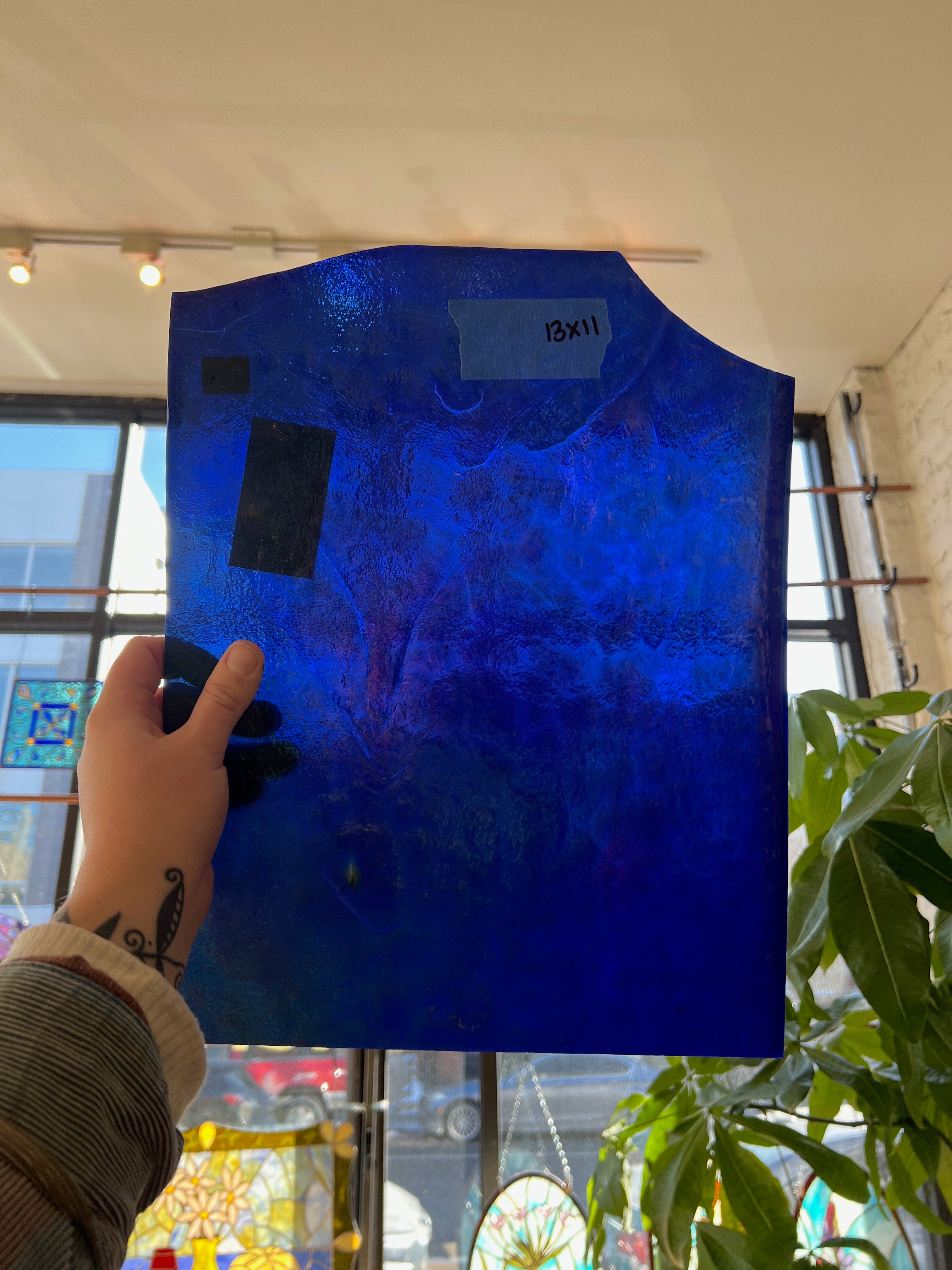 Blue textured piece of glass held by a person indoors with windows and plants in the background