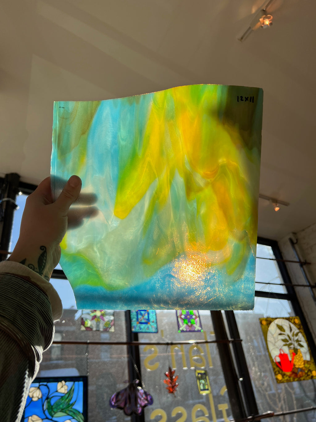 Person holding a piece of blue and yellow swirled stained glass in front of a blurred window.
