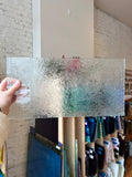 Person holding a sheet of textured glass against a brick wall.