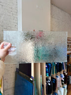 Person holding a sheet of textured glass against a brick wall.
