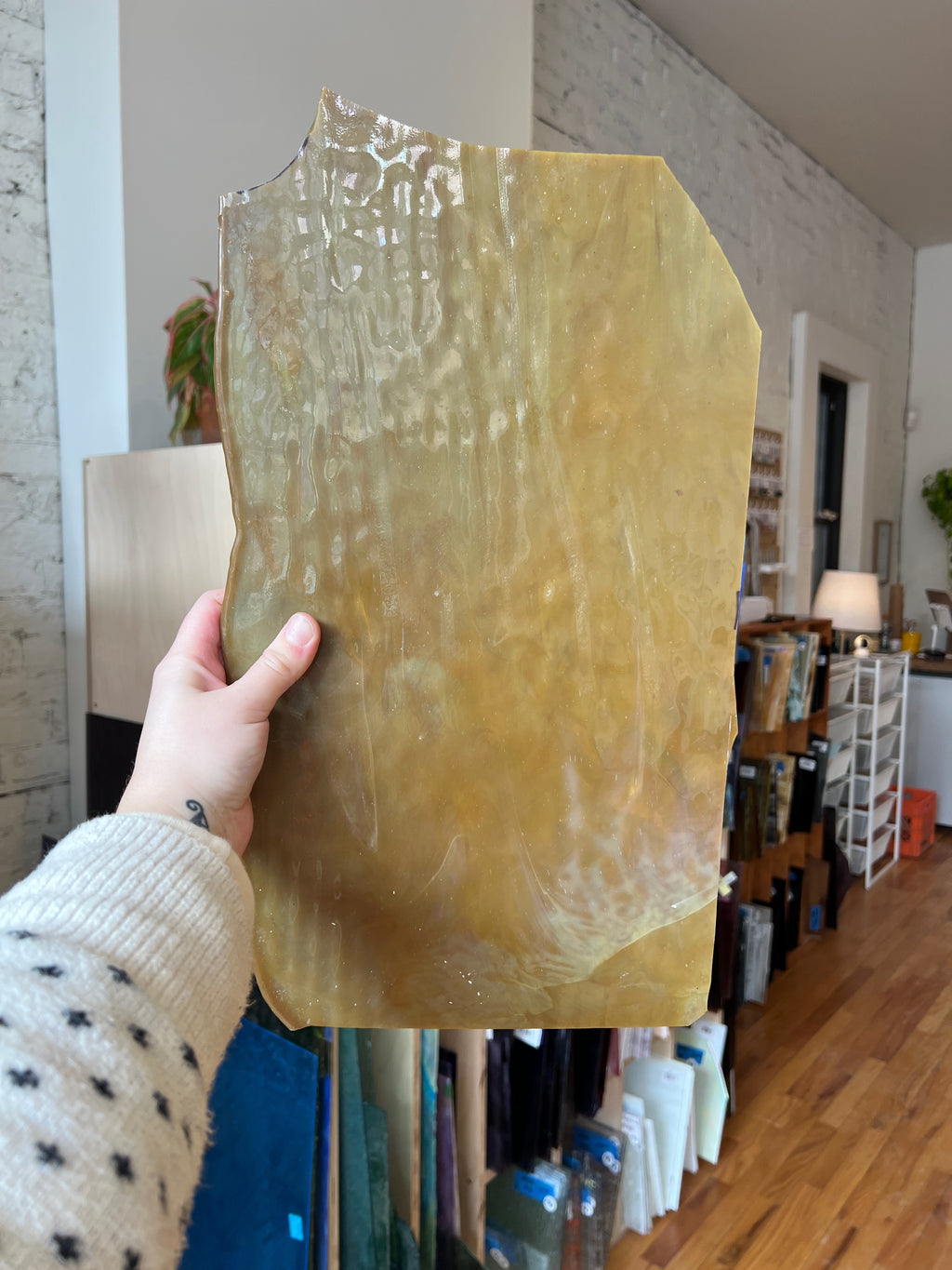 Person holding a piece of tan and white swirled stained glass in front of a blurred interior.
