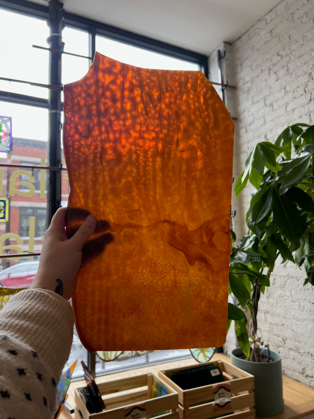 Person holding a piece of amber stained glass in front of a blurred window.