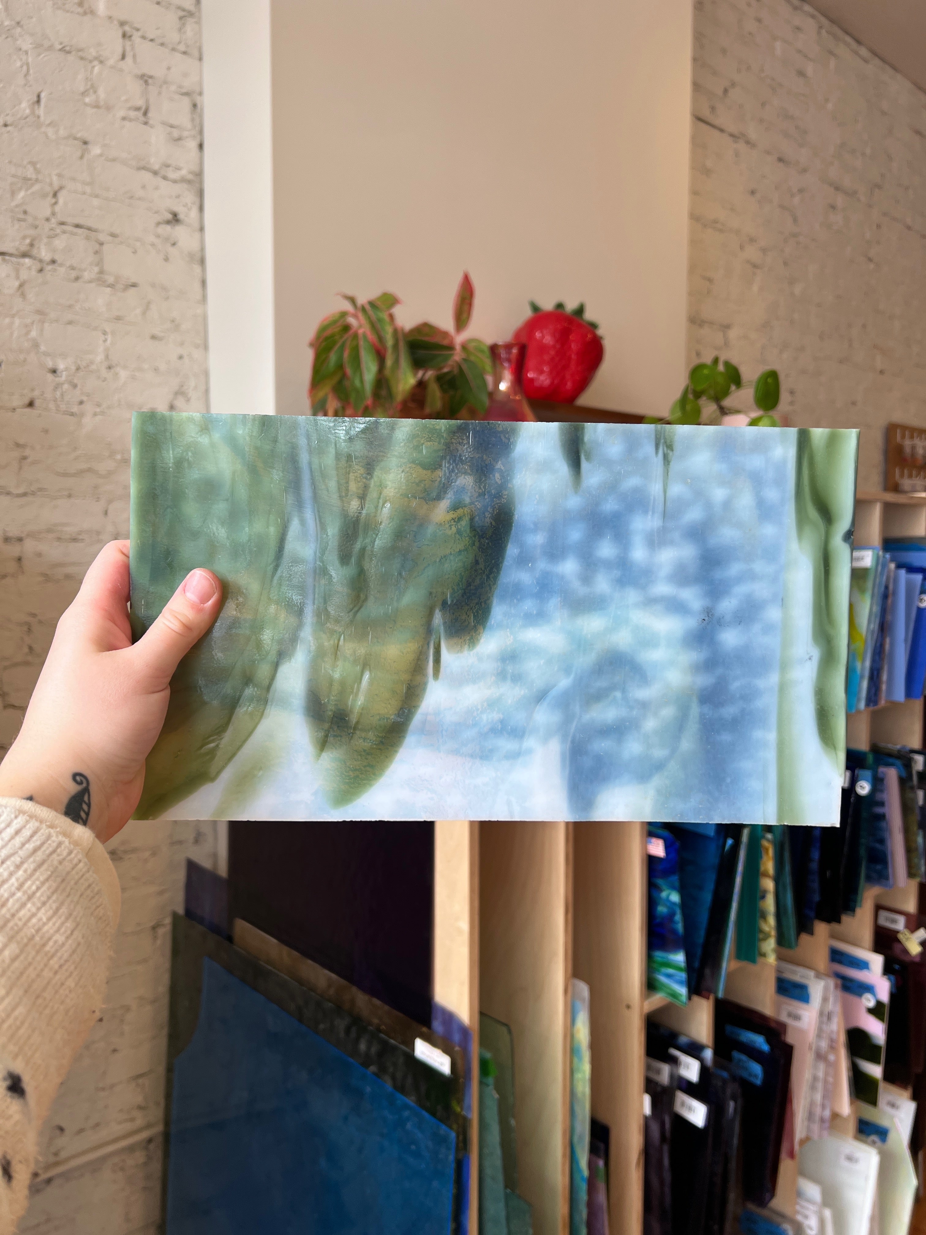 Person holding a piece of green and white swirled stained glass in front of a blurred interior.