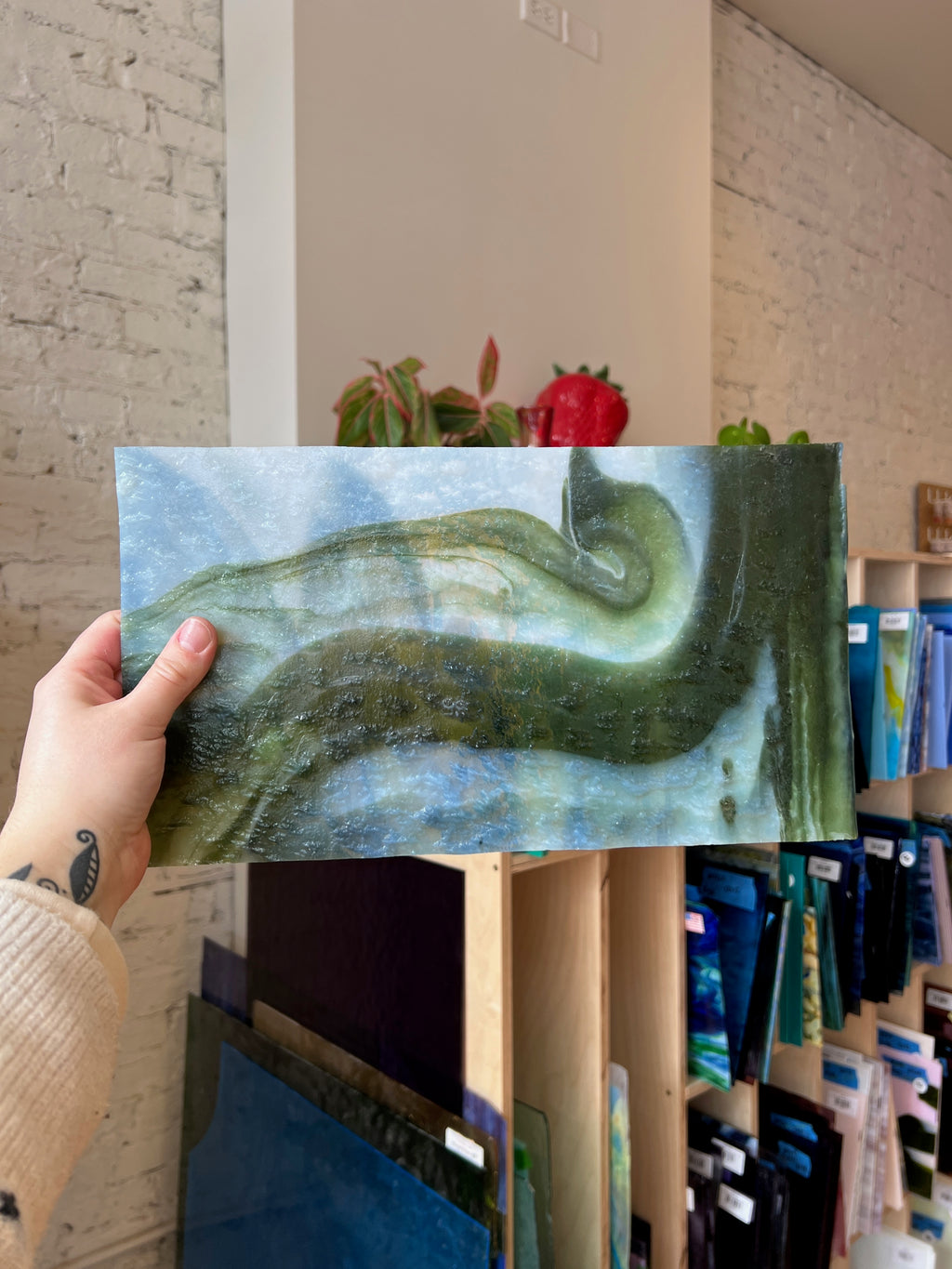 Person holding a piece of green and white swirled stained glass in front of a blurred interior.