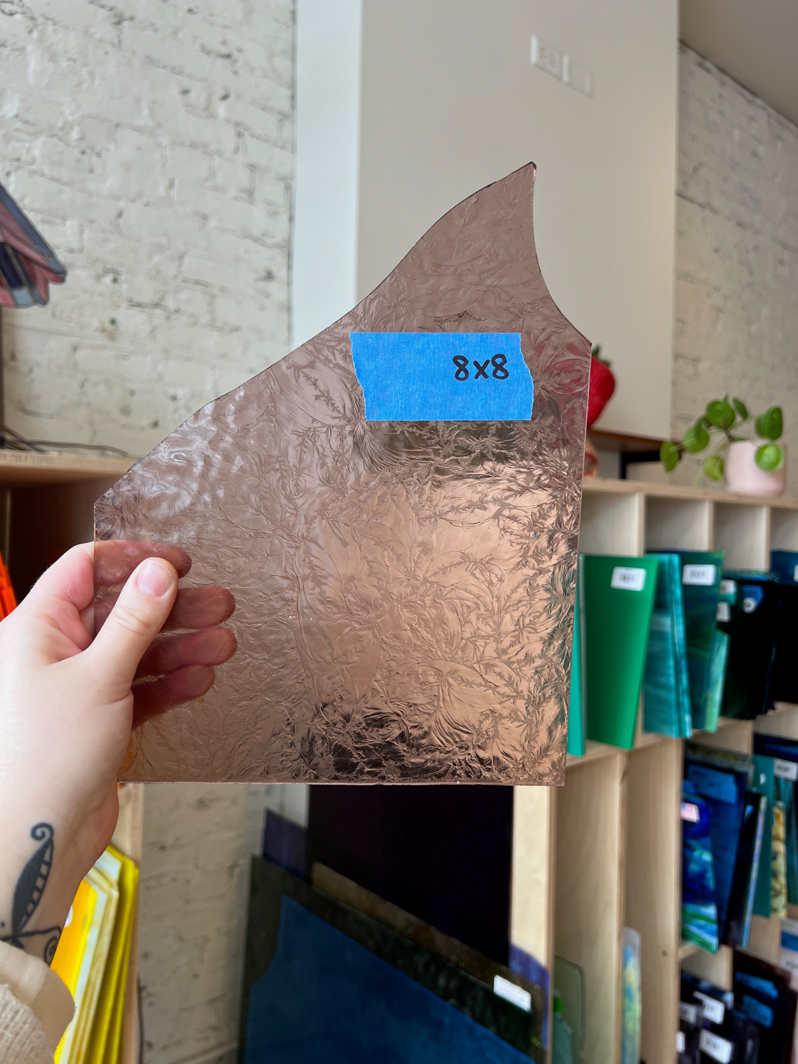 Person holding a lilac textured piece of stained glass in front of a blurred interior. 