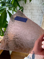 Person holding a lilac glue chip textured piece of stained glass in front of a blurred interior. 