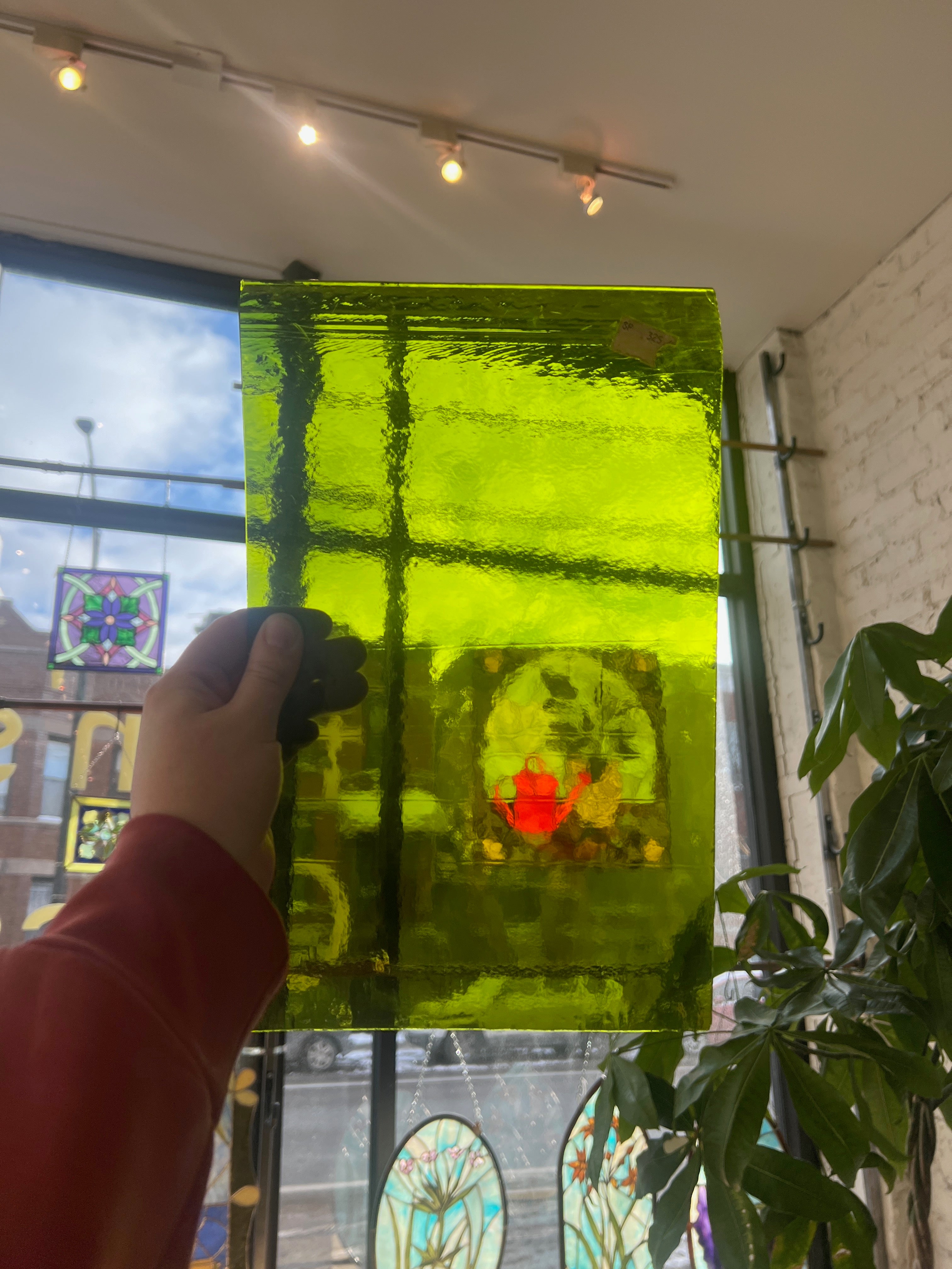 Person holding a green transparent piece of stained glass in front of a blurred sunny window. 