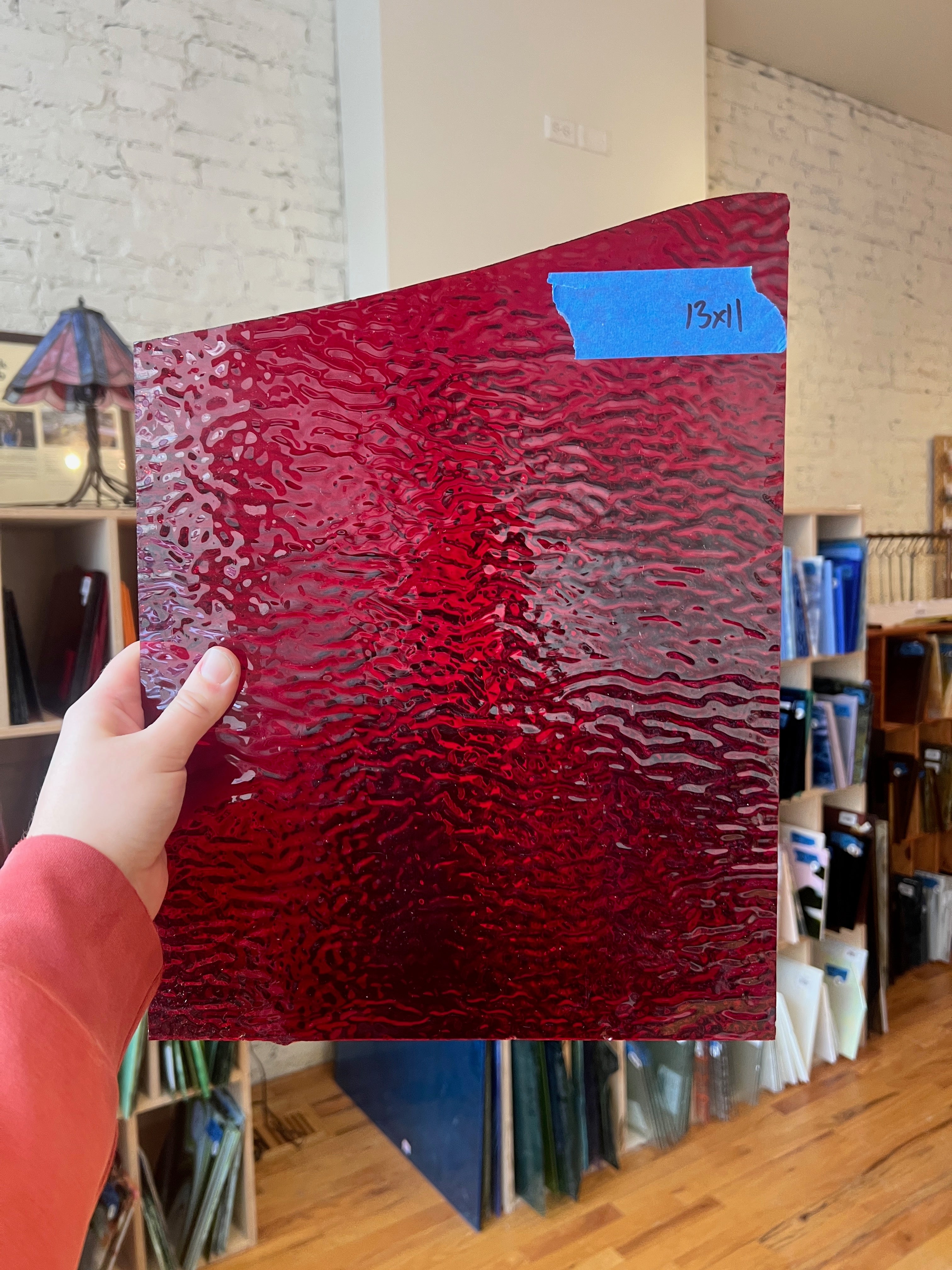 Person holding a red textured piece of stained glass in front of a blurred interior. 
