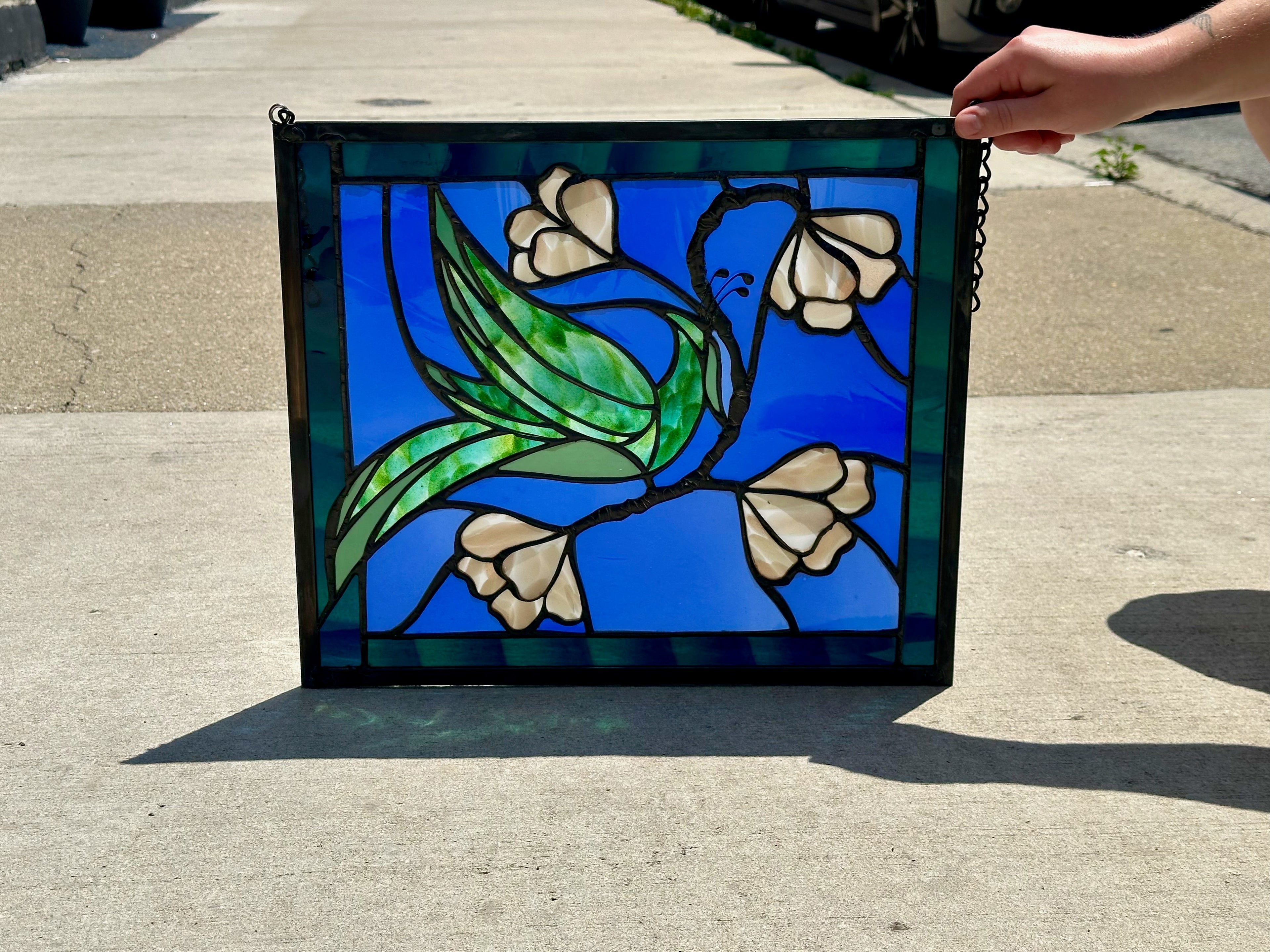Stained glass panel with floral design held by a person on a concrete surface