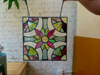 Stained glass panel with colorful floral design hanging against a brick wall.