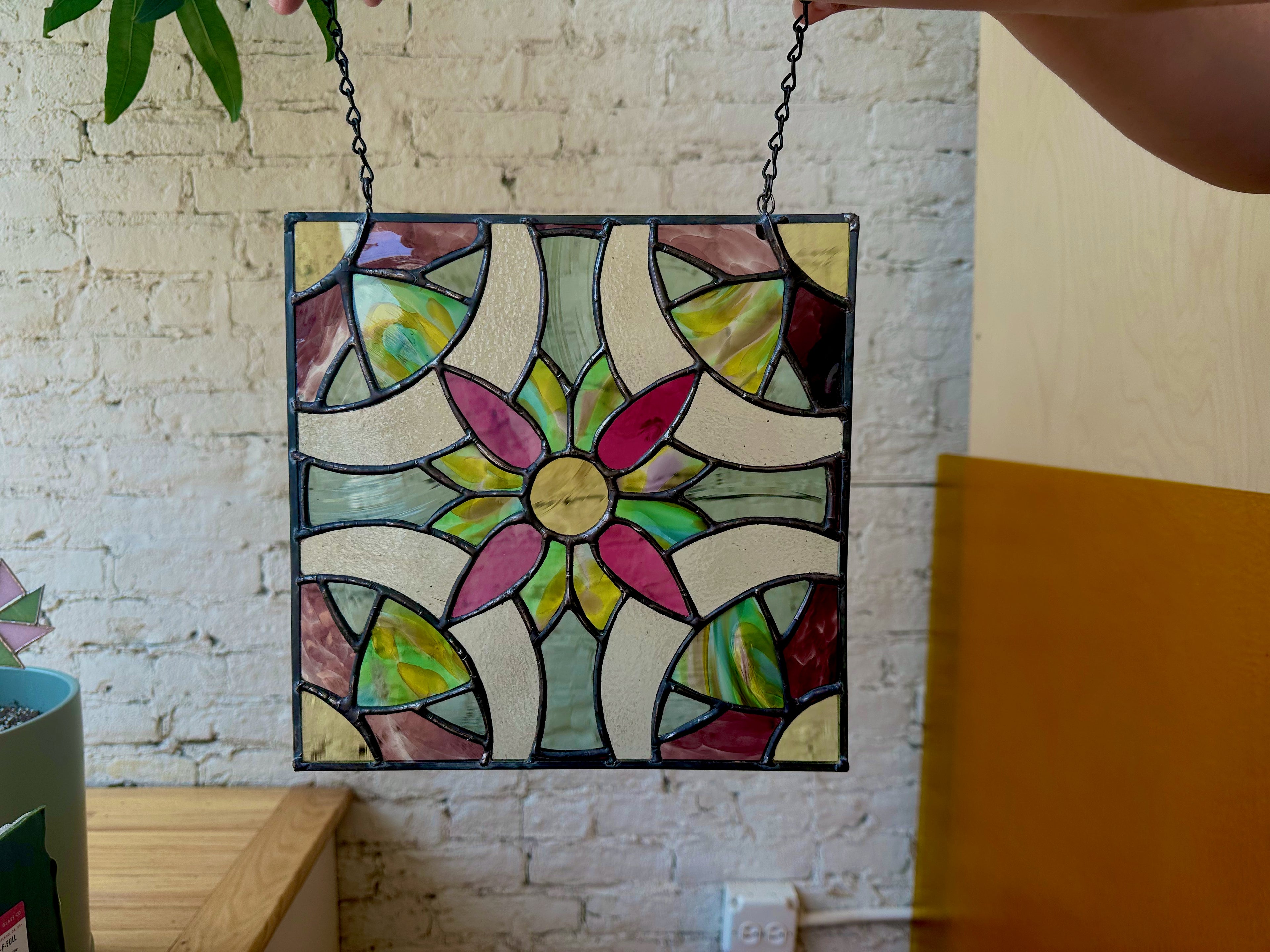 Stained glass panel with colorful floral design hanging against a brick wall.