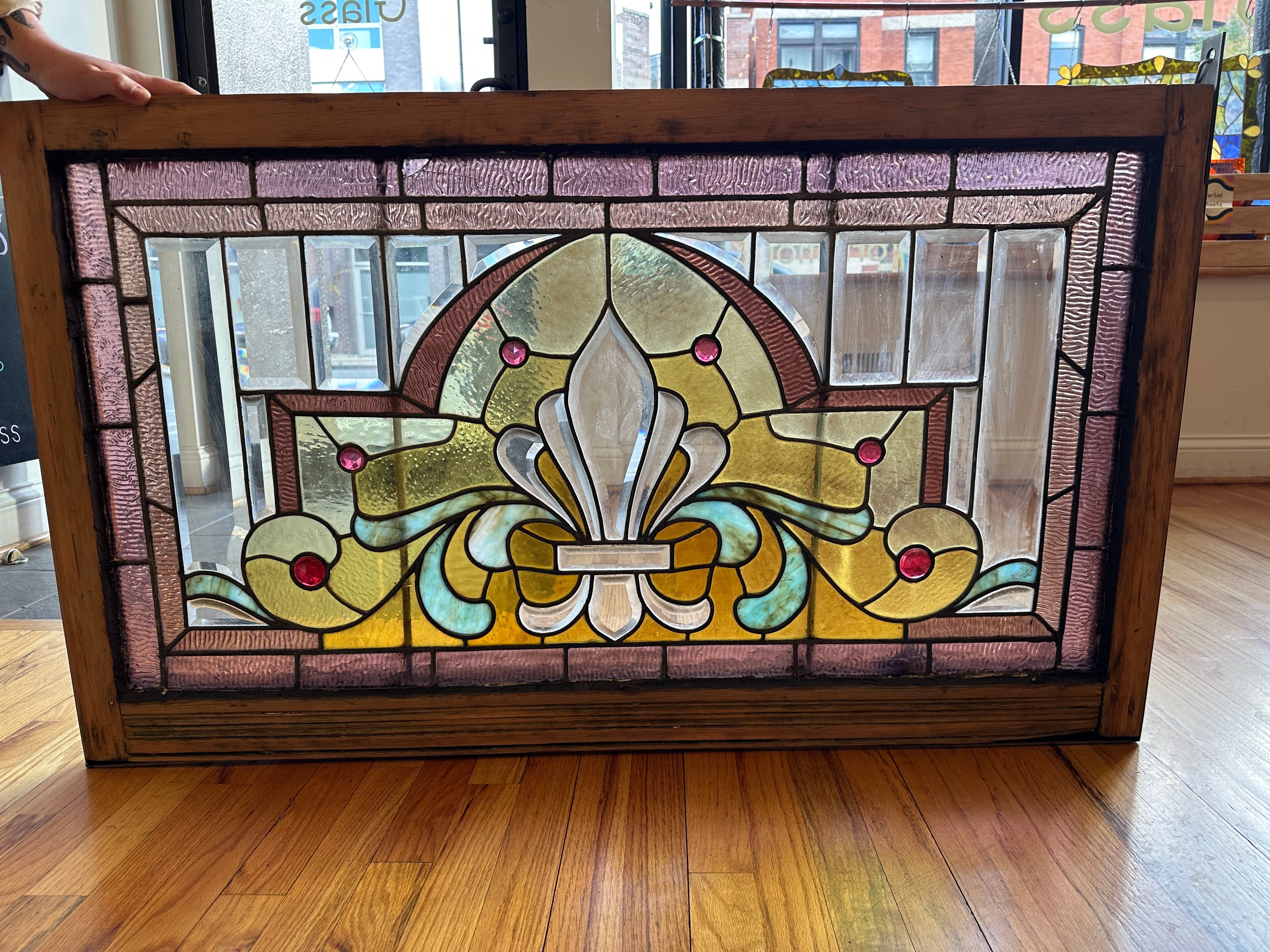 Stained glass panel with floral design in a wooden frame on a wooden floor.