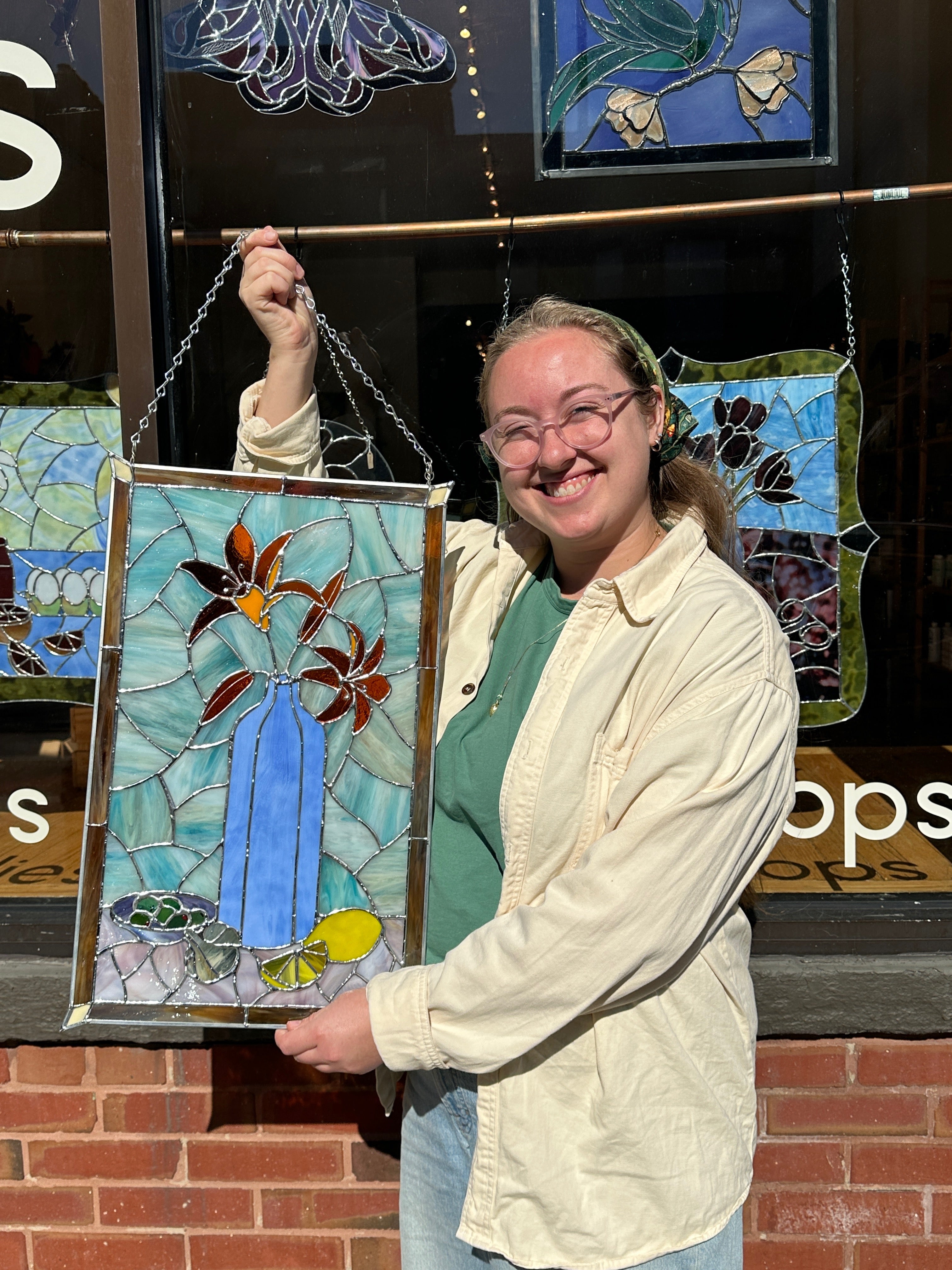 Person holding a stained glass panel in front of a store with more stained glass art on display.
